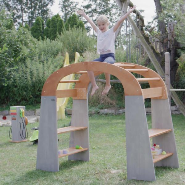 Ein Kind spielt freudig mit dem Outdoor Spielständer draußen im Garten