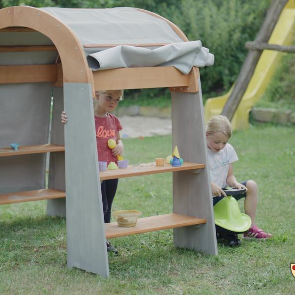 Kinder spielen draussen im Garten mit dem Spielhaus geschützt und dem Sonnensegel Eis verkaufen